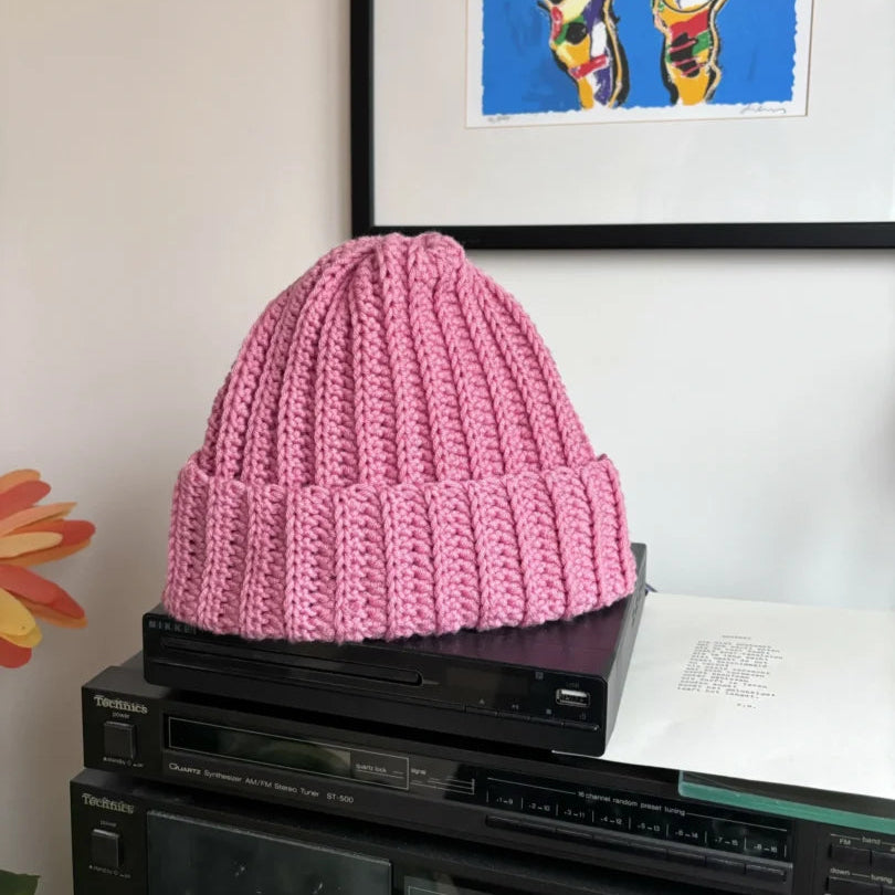 Een gehaakte roze muts van Haakspot op een bureau.