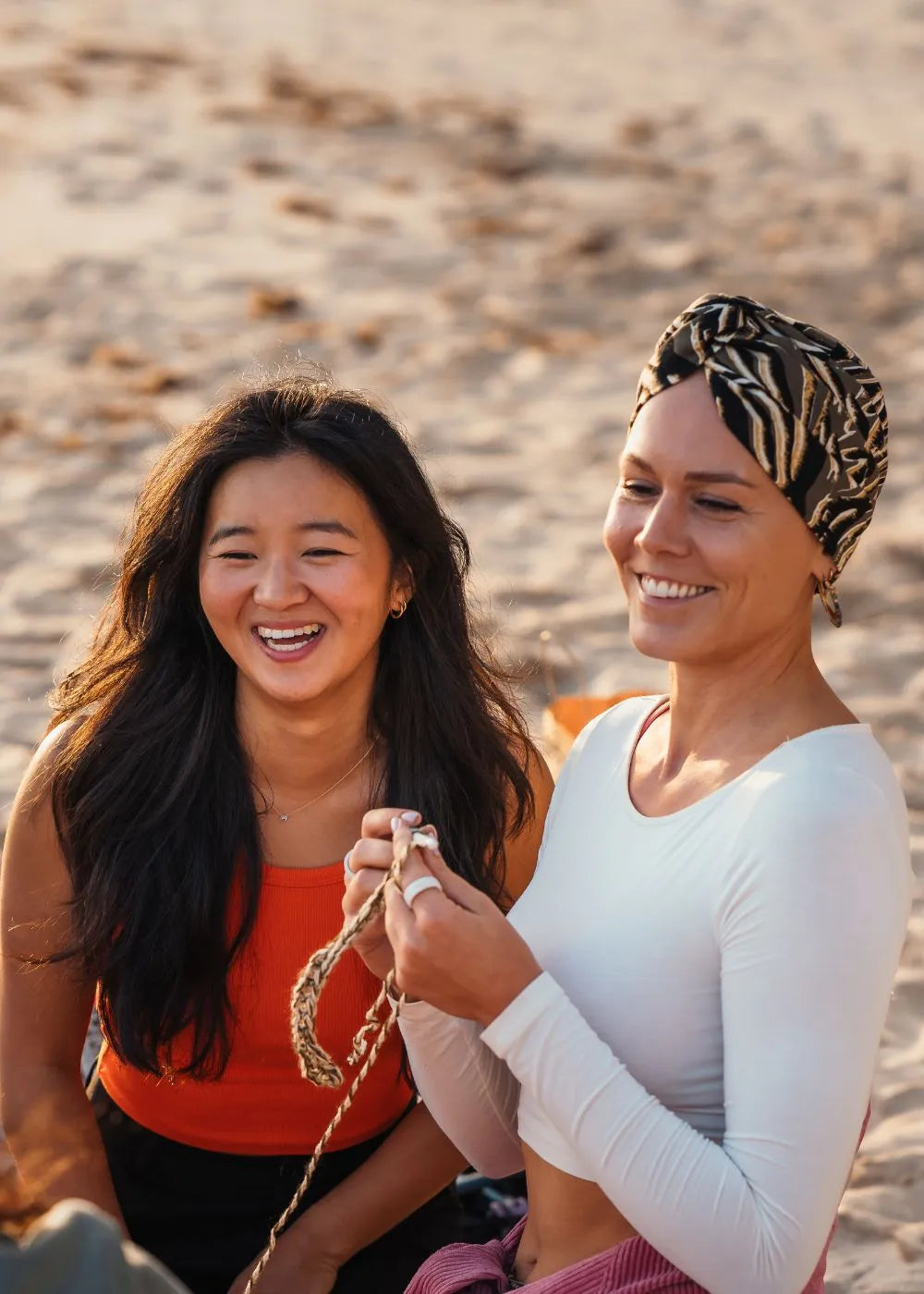 Twee jonge vrouwen haken samen op het strand en lachen.